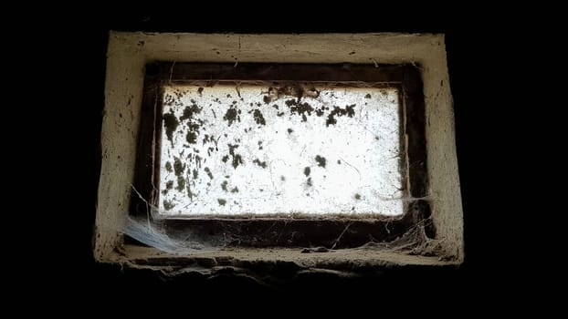 a small rectangular dirty and dusty web window in a large basement. White light penetrates the dark basement