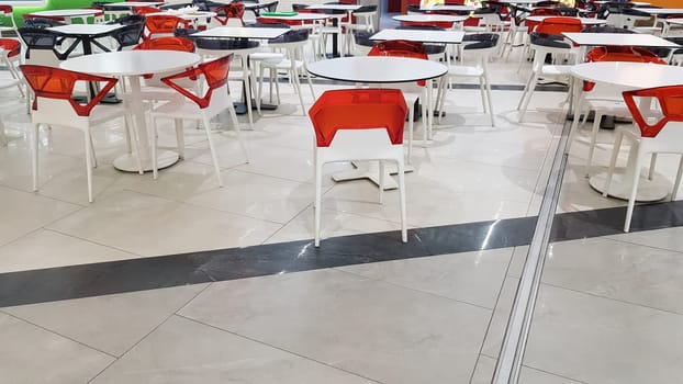 food area with plastic white and red tables and chairs in a mall without people.