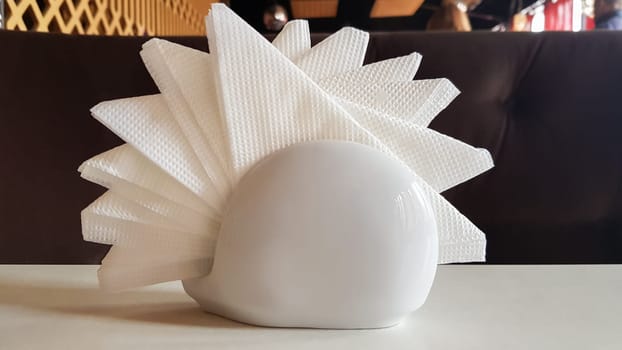 A table in a cafe and restaurant. White napkins in a ceramic napkin holder. Hotel dining table with napkins. A paper napkin is placed in a glass on a table in the banquet room