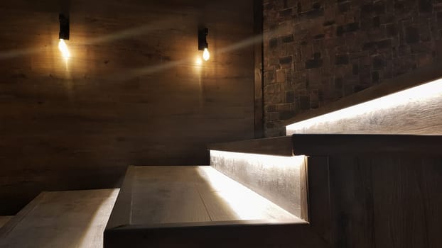 Illuminated staircase with wooden steps and illuminated at night in the interior of a large house.