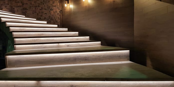 Illuminated staircase with wooden steps and illuminated at night in the interior of a large house.