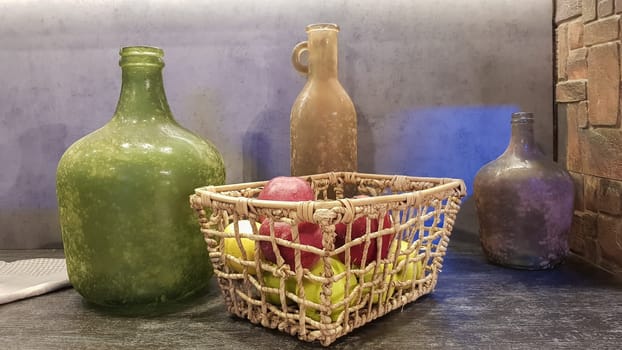 Large glass vases, a basket with apples and plates in the interior of a modern kitchen. The combination of wood and concrete in the design. Modern style dining kitchen.