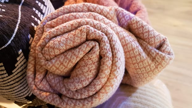 Knitted and warm blankets are folded and laid in a wicker basket near the fireplace. Cozy interior in the house. Details of a modern cozy interior.