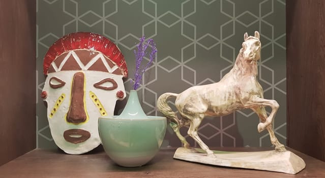 Ukraine, Kiev - June 10, 2020. Ceramic figurines and figures decoration or symbol in the home interior. Mask, a small vase, a horse on a shelf of a wooden cabinet.