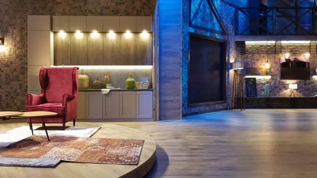 Ukraine, Kiev - June 10, 2020. Modern living room of a large house with a kitchen, fireplace, green sofa and red soft chairs, steps to the second floor, ice lights and lamps, decoration elements.