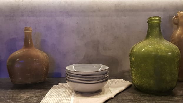 Large glass vases, a basket with apples and plates in the interior of a modern kitchen. The combination of wood and concrete in the design. Modern style dining kitchen.