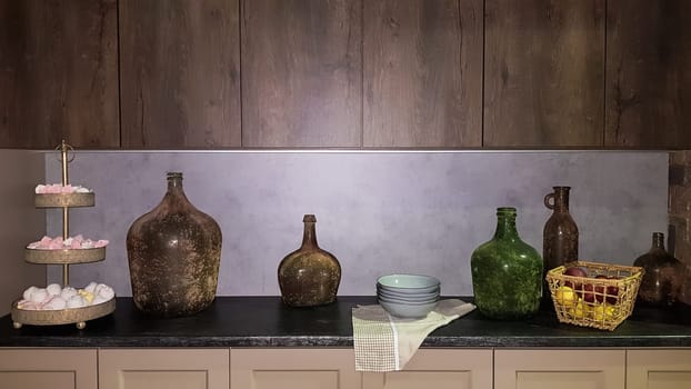Large glass vases, a basket with apples and plates in the interior of a modern kitchen. The combination of wood and concrete in the design. Modern style dining kitchen.