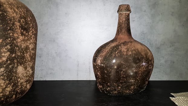 large vintage vases or jugs of colored glass as decoration elements in a modern interior near a gray concrete wall. Decoration of an apartment or house
