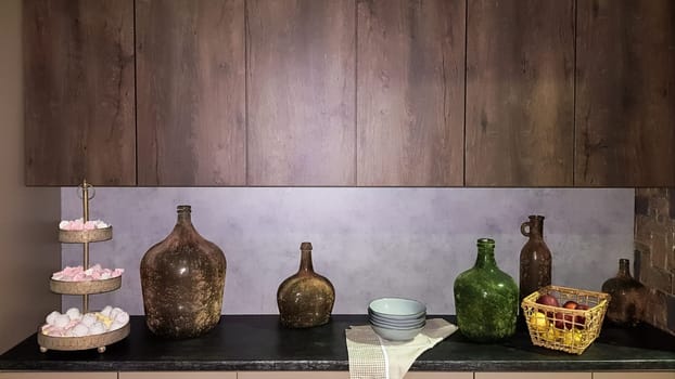 Large glass vases, a basket with apples and plates in the interior of a modern kitchen. The combination of wood and concrete in the design. Modern style dining kitchen.