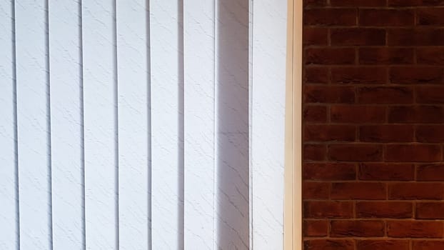 Large window with vertical white or gray blinds, loft, brick wall, industrial interior. Sunlight from a window on brick walls in a room or office
