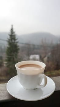 White cup of coffee on abstract nature background. One coffee mug on the balcony with a view of the nature behind. Ceramic cup with a drink on the hotel balcony.
