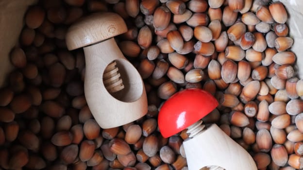 A lot of hazelnuts on burlap with a wooden mushroom-shaped nutcracker. Hazelnuts food background. A large number of nuts in a bag with crackers. Chopper walnuts and raw healthy food