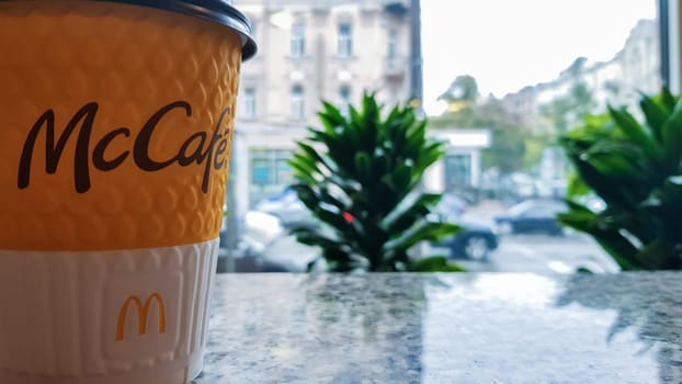 McDonald's logo on a yellow paper cup with hot McCafe coffee near the window. Fast food chain. Breakfast, coffee time. Ukraine, Kiev - September 30, 2020