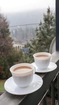Two coffee cups on a balcony with mountain landscape in the morning. Two cups of morning coffee, standing on the side of the balcony, with a magical view of the autumn forests