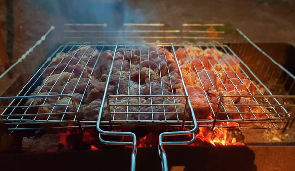 The process of cooking shish kebab on the grill. Juicy and fragrant meat languishes on fire and smoke. Countryside picnic concept at night. Appetizing and nutritious picnic dish in the open air
