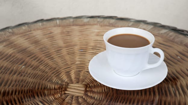 Hot aromatic coffee with milk. Freshly prepared drink is served in a modern cup on a light wicker table