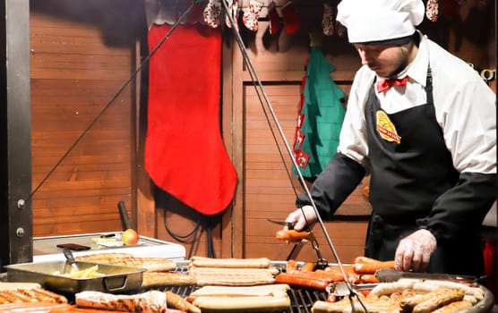 Ukraine, Kiev - January 3, 2019: a chef cooks a barbecue on the grill, street food, food festival. Fresh sausage and grilled hot dogs outdoors. A man is preparing street food of German cuisine.