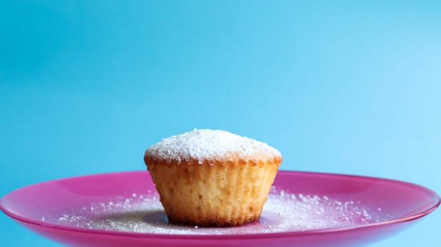 One curd sprinkled with powdered sugar on a pink plate, on a blue background, side view. Dessert, a small cupcake. Food concept. white baked cookies with an airy texture. Copy space.
