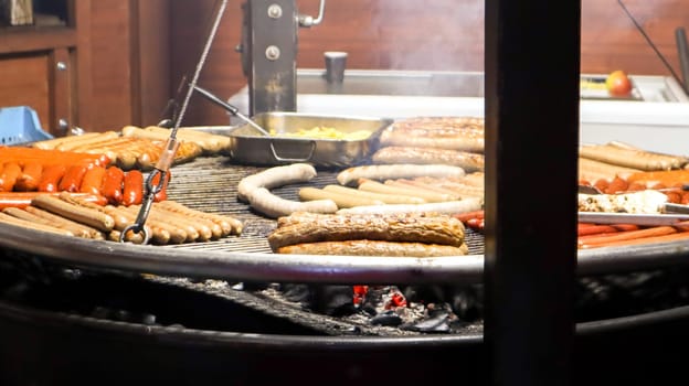 Fried sausages. Street eatery. Many grilled sausages on a large round barbecue grill at a street food festival. Barbecue grill at food stall Christmas market