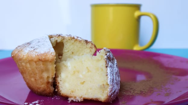 Side view of one cottage cheese sprinkled with icing sugar on a pink plate next to a yellow cup of coffee or tea. Dessert, a small cupcake. white baked cookies with an airy texture. Copy space.