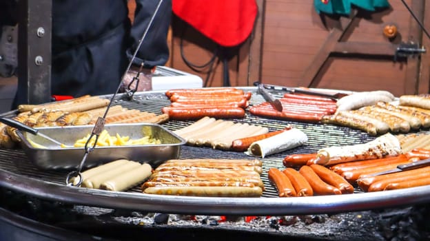 Fried sausages. Street eatery. Many grilled sausages on a large round barbecue grill at a street food festival. Barbecue grill at food stall Christmas market
