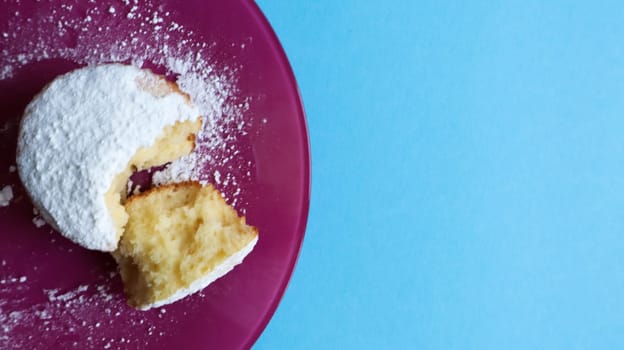 Sprinkle one cottage cheese with powdered sugar on a pink plate, on a blue background, top view. Dessert, a small cupcake. Food concept. white baked cookies with an airy texture. Copy space.
