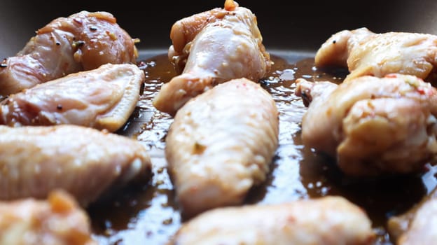 Raw pickled chicken teriyaki wings in a pan before frying. A few raw chicken wings on a baking sheet. Chicken meat in oil and in spices in a black pan, the cooking process