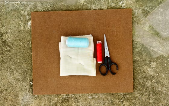 Group of sewing tools and items for knitting and weaving placed on a brown colour woven paper board. DIY Art and craft background concept.