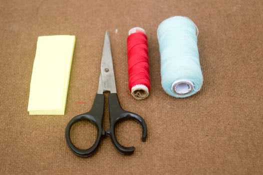 Group of sewing tools and items for knitting and weaving placed on a brown colour woven paper board. DIY Art and craft background concept.