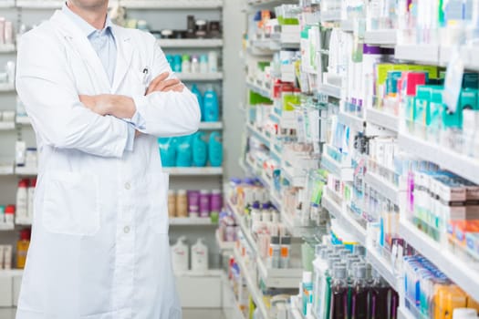 Portrait of smiling mid adult male pharmacist standing arms crossed in pharmacy