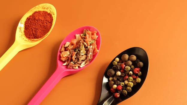 Various spices in plastic spoons on a brown background. Copy space. A mixture of peppers, red smoked paprika, seasoning twelve vegetables