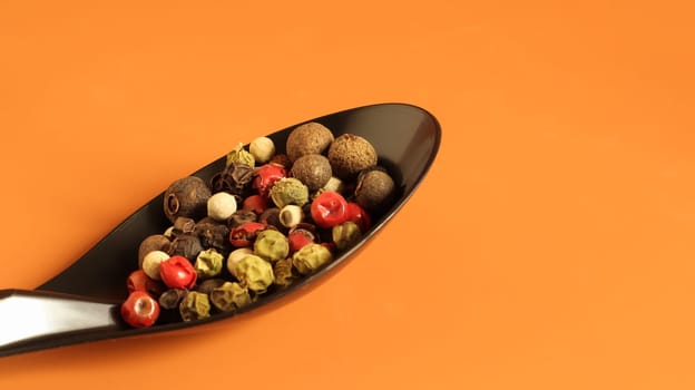 A mixture of hot, red, black, white and green peppers in a black spoon. Isolated on a brown background