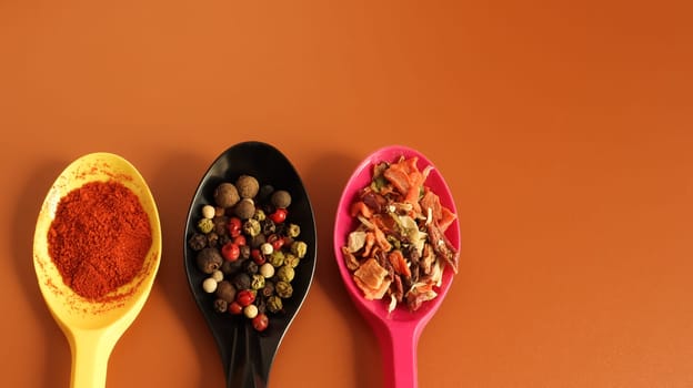 Various spices in plastic spoons on a brown background. Copy space. A mixture of peppers, red smoked paprika, seasoning twelve vegetables