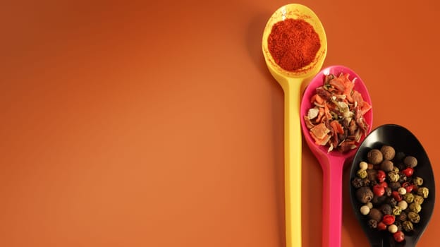 Various spices in plastic spoons on a brown background. Copy space. A mixture of peppers, red smoked paprika, seasoning twelve vegetables