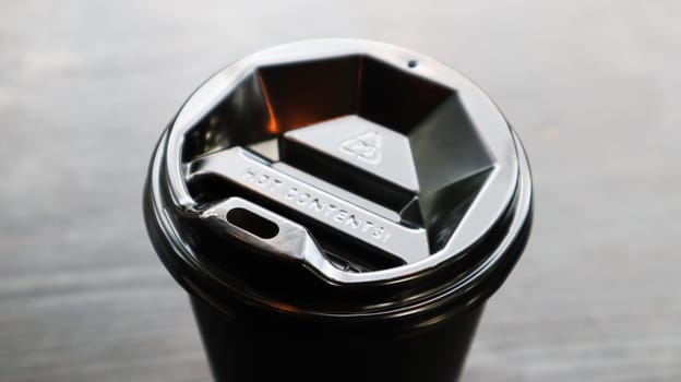 Black plastic coffee cup cover, top view. Takeaway coffee cup black background. Disposable cup close-up on a wooden table. Minimalist style.