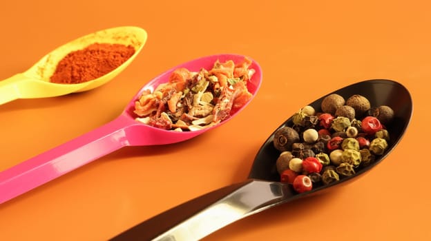 Various spices in plastic spoons on a brown background. Copy space. A mixture of peppers, red smoked paprika, seasoning twelve vegetables