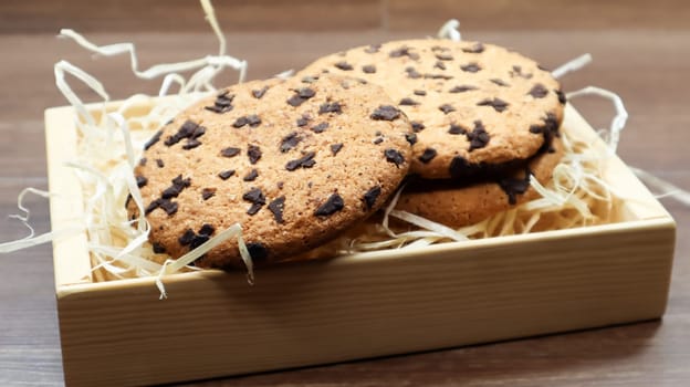 American chocolate chip cookies on a brown wooden table close-up in a box. Traditional rounded crunchy dough with chocolate chips. Bakery. Delicious dessert, pastries. Rural still life
