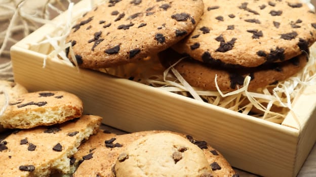 American chocolate chip cookies on a brown wooden table close-up in a box. Traditional rounded crunchy dough with chocolate chips. Bakery. Delicious dessert, pastries. Rural still life