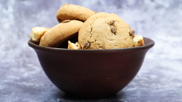 Soft freshly baked cookies with chocolate chips in a brown earthenware plate on gray marble. American traditional sweet pastry pastry, delicious homemade dessert. Culinary background