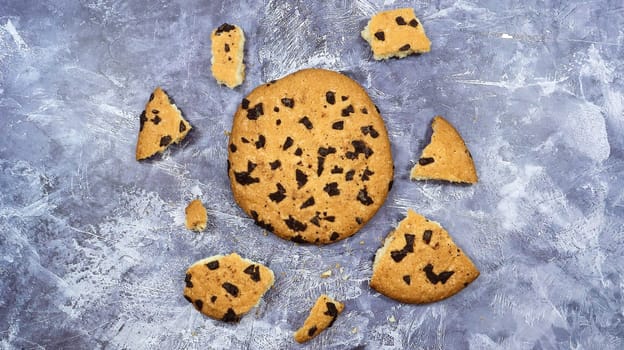 One soft freshly baked chocolate chip cookie with crumbs and chunks on a gray marble kitchen countertop. American traditional pastry, dessert. Delicious sweet food. Flat lay