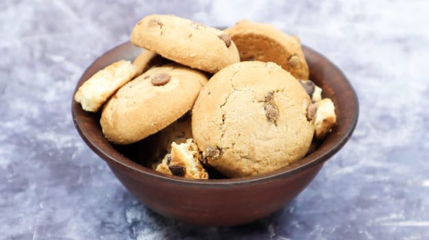 Soft freshly baked cookies with chocolate chips in a brown earthenware plate on gray marble. American traditional sweet pastry pastry, delicious homemade dessert. Culinary background