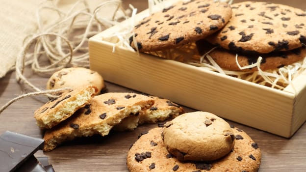 American chocolate chip cookies on a brown wooden table close-up in a box. Traditional rounded crunchy dough with chocolate chips. Bakery. Delicious dessert, pastries. Rural still life