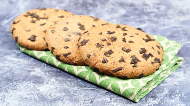 American chocolate chip cookies on a green napkin on a gray background. Traditional round crispy dough with chocolate chips. Bakery. Delicious dessert, pastries