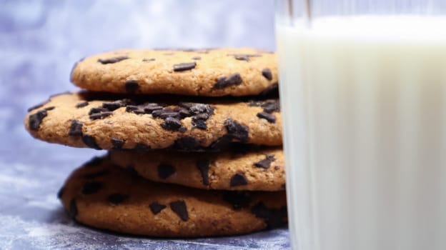 American chocolate chip cookies stacked on top of each other with milk in a glass on a gray background. Traditional rounded crunchy dough with chocolate chips. Bakery. Delicious dessert, pastries