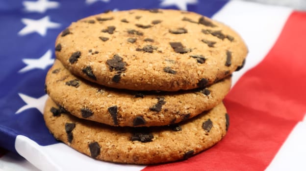Patriotic cookies. Three rounded traditional chocolate chip cookies on the background of the flag of the United States of America. Delicious sweet pastries, dessert. America's favorite treat