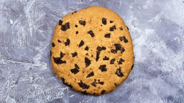 One soft, freshly baked chocolate chip cookie on a gray marble kitchen countertop. American traditional pastry, dessert. Delicious sweet food. Flat lay.