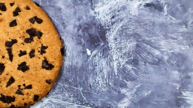 One soft, freshly baked chocolate chip cookie on a gray marble kitchen countertop. American traditional pastry, dessert. Delicious sweet food. Flat lay. Copy space.