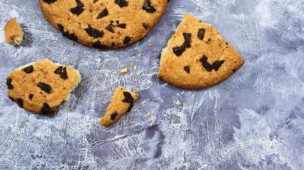 One soft freshly baked chocolate chip cookie with crumbs and chunks on a gray marble kitchen countertop. American traditional pastry, dessert. Delicious sweet food. Flat lay