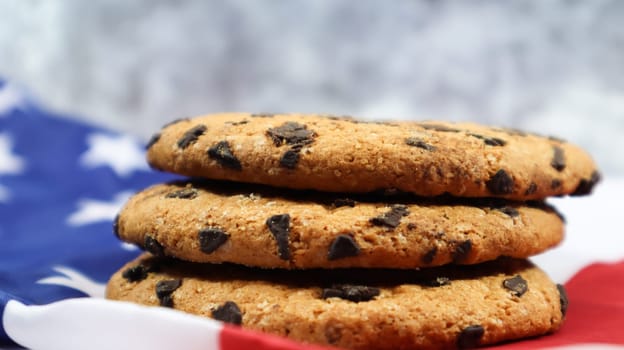 Patriotic cookies. Three rounded traditional chocolate chip cookies on the background of the flag of the United States of America. Delicious sweet pastries, dessert. America's favorite treat