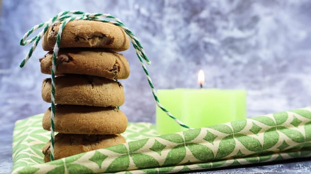 American chocolate chip cookies in a stack tied with thread on a green napkin and a candle. Traditional rounded crunchy dough with chocolate chips. Bakery. Delicious dessert, pastries